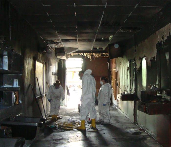 3 people in Tyvek suits and yellow boots walking around a hallway from a destroyed building from a fire 
