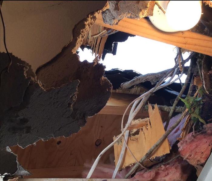 A hole in the roof of a home with wires and wood hanging down from it