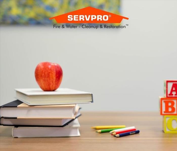A table with books and an apple on them and the SERVPRO logo at the top.